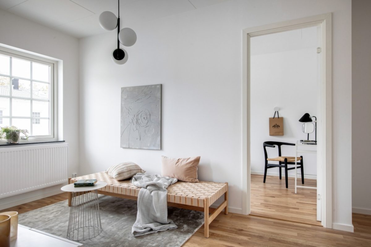 Ett ljust och minimalistiskt rum på Myntgatan med en träbänk, ett litet vitt soffbord, och en modern taklampa.